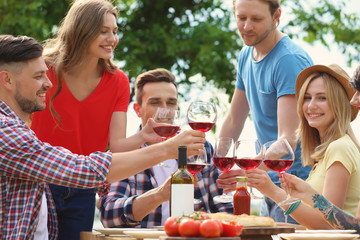 Young people with glasses of wine at table outdoors. Summer barbecue