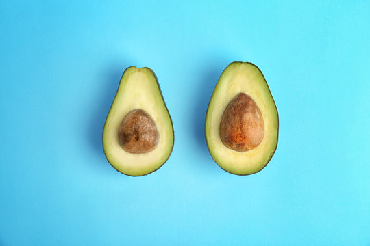 Halves of ripe avocados on color background, top view
