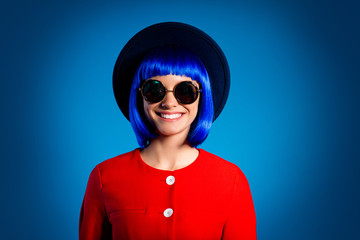 Portrait of glamorous positive girl with beaming toothy smile in summer glasses red outfit looking at camera isolated on blue background with light and shadow