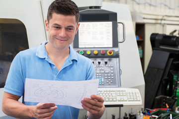 Male Engineer With Technical Drawing Operating CNC Machine In Factory