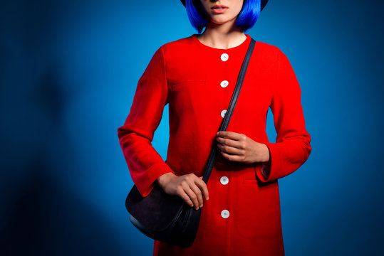 Cropped portrait of fashionable pretty woman in red outfit with black bag on shoulder isolated in bright blue background. Wear cloth concept