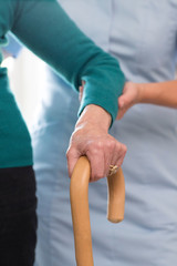 Senior Womans Hands On Walking Stick With Care Worker In Background