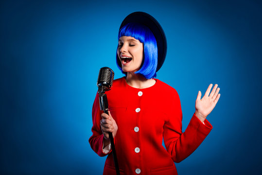 Portrait of creative active artist in headwear red outfit singing with open mouth close eyes in microphone isolated on bright vivid blue background. Comfort relax leisure concept