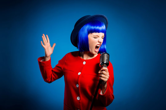 Portrait of professional emotional artist in head wear singing hard rock with wide open mouth and close eyes gesturing with hand isolated on bright blue background. Art jazz opera concept