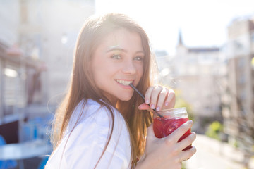 Outside portrait of charming pretty young lady with long hair dressed white t-shirt drinks summer coctail amd looking at camera with adorable smile, true happt emotions, positive mood