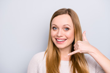 Portrait of friendly cute girl with beaming smile gesturing telephone sign with fingers near ear,...