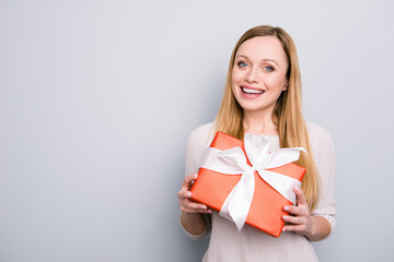 Portrait with copyspace empty place of cheerful positive girl having gift box in red package with white bow isolated on grey background looking at camera