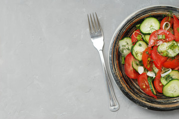 Tomato and cucumber salad vegan food with fork gray textured cement background