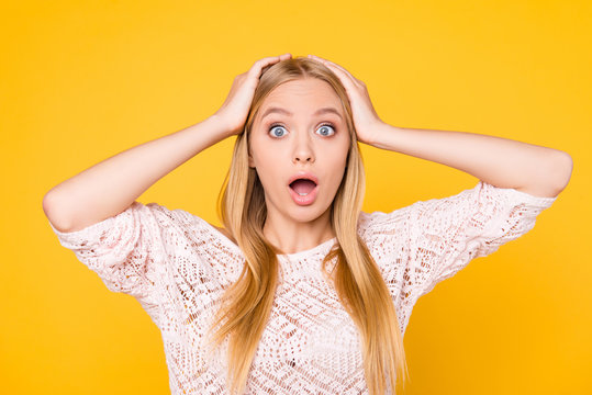 Portrait of shocked scared girl having panic holding two palms on cheeks looking at camera with wide open mouth and eyes isolated on yellow background