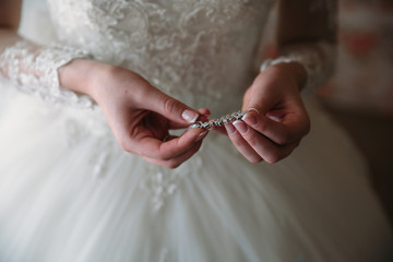 Close-up earrind in the hands of the bride on her white wedding dress background. Concept of jewelry. Morning preparation of the bride for marriage.