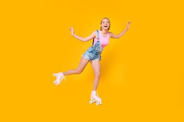 Fototapeta na wymiar Full-length portrait of glad excited girl riding on roller skates with one leg keeping balance enjoying recreation exercise isolated on yellow background, sporty fit people concept