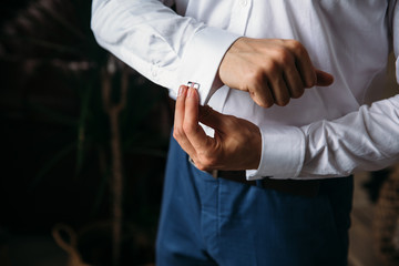 Close-up groom hands hold cufflinks. Elegant gentleman clother, white shirt and black belt. concept...