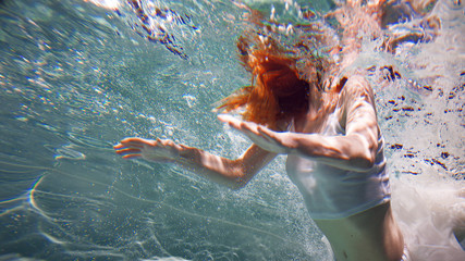 Underwater girl. Beautiful red-haired woman in a white dress, swimming under water. © Ulia Koltyrina
