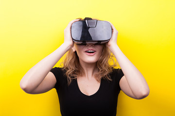 Beautiful woman enjoying virtual reality experience on yellow background in studio photo