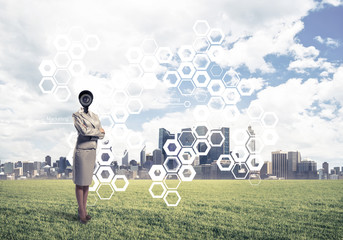 Camera headed woman standing on green grass against modern citys