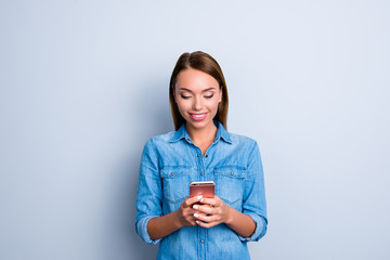 Portrait of modern addicted girl in jeans shirt having smart phone in hands checking email using wifi 3G internet isolated on grey background