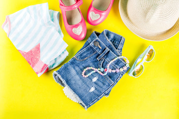 Summer vacation concept, summer child's cloth set - kids shorts, T-shirt, hat, sun glasses, bracelet necklace, sneakers, bright yellow background above flat lay copy space