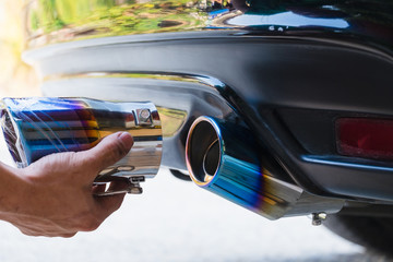 Hand holding colorful rainbow color exhaust pipe of car.