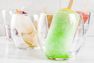 Summer party food ideas, frozen boozy alcohol cocktails popsicles - Prosecco, Vodka lime mojito, Champagne, Bellini, Margarita, Negroni etc white marble table copy space