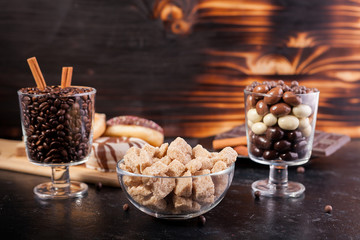 Candies, brown sugar, donuts and coffee on dark vintage wooden background