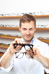 Twarzowe modne okulary. Mężczyzna wybiera oprawki okularowe w salonie optycznym