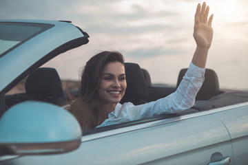 Portrait of happy young woman is enjoying trip by convertible personal transport. She is waving arm and smiling 