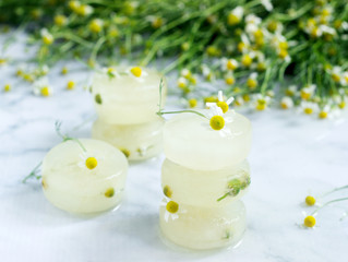 Obraz na płótnie Canvas Ice cubes of chamomile tea and chamomile for cosmetic purposes on a background of a bouquet of daisies.