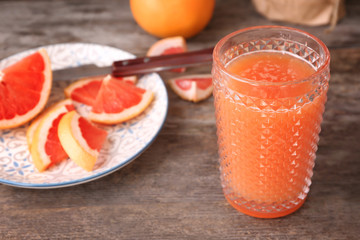 Glass with delicious citrus juice and fresh grapefruit on table