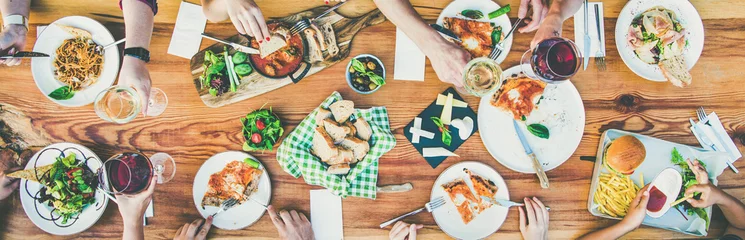 Fotobehang Family or friends summer party or outdoor dinner. Flat-lay of group of people at big table in cafe eating verious food together. Summer gathering or celebration concept © sonyakamoz