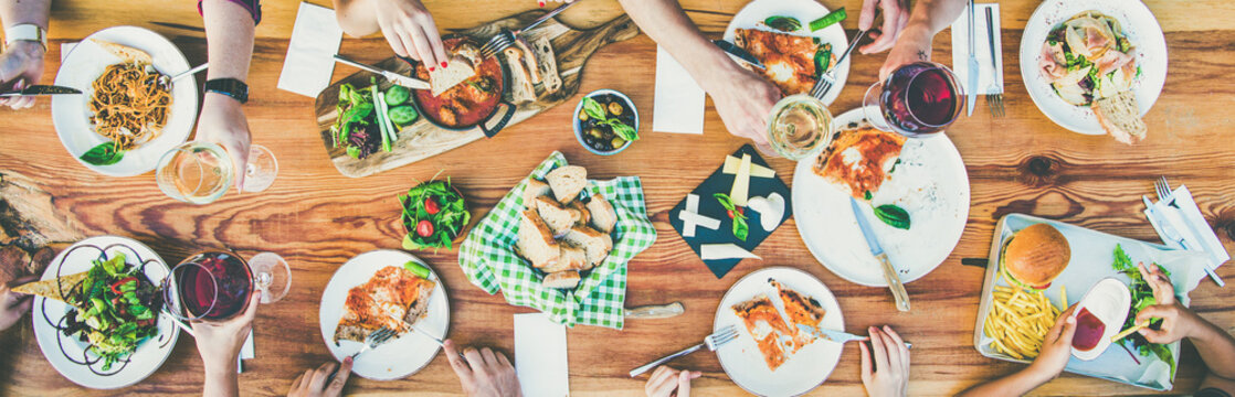 Family or friends summer party or outdoor dinner. Flat-lay of group of people at big table in cafe eating verious food together. Summer gathering or celebration concept