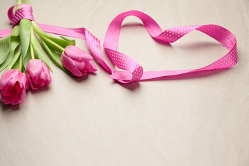 Beautiful tulips and heart made of ribbon on light background