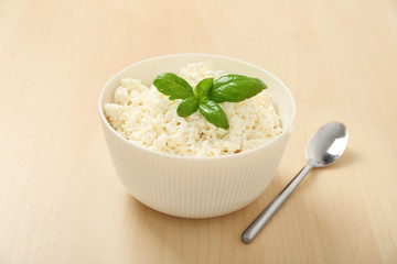 Bowl with tasty cottage cheese and basil on light background