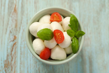 Bowl with mozzarella cheese balls, cherry tomatoes and basil on wooden background