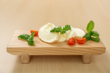 Mozzarella cheese served with cherry tomatoes and basil on wooden stand