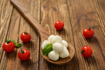 Mozzarella cheese balls, cherry tomatoes and basil on wooden background