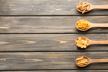 Naklejka premium Spoons with different uncooked pasta on wooden background