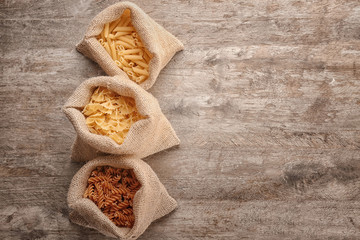 Bags with different uncooked pasta on wooden background