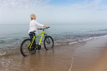 Fototapeta premium Woman walking in the sea wheeling a bicycle