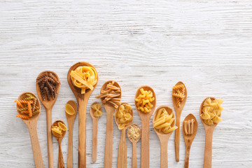Wooden spoons with uncooked pasta on light background