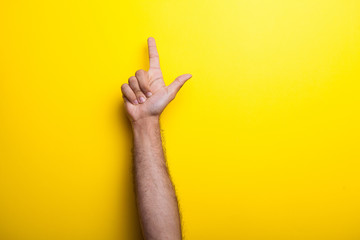 Male hands points up on yellow background. Studio photo
