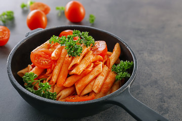 Pan with tasty penne pasta in tomato sauce on table