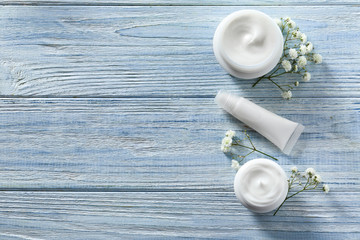 Flat lay composition with skin care cosmetics and flowers on wooden background