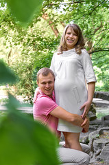 Handsome man is listening to his beautiful pregnant wife's tummy belly and smiling. Husband listening to his wife's belly. Happy pregnant family funny.