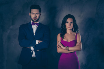 Portrait of brutal mr with stubble in tuxedo with bowtie and charming pretty woman in dress with bijouterie attractive couple holding arms crossed looking at camera isolated on grey background