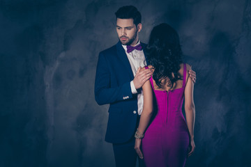 Rear view of pretty brunette woman with curly hair booty bum harsh man in tux with bow holding hands on shoulders of lover attractive couple isolated on grey background with copy space empty place