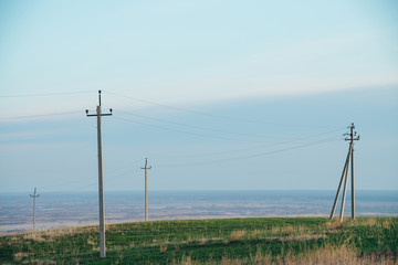 Atmospheric landscape with power lines in green field under blue sky. Background image of electric pillars with copy space. Wires of high voltage above ground. Electricity industry.