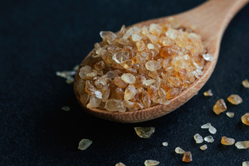 Natural brown sugar or no bleach sugar on wood spoon on black granite table in close up view macro concept with copy space. Sweet seasoning for good health. Ingredient prepared for cooking or bakery.