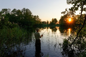 Fisherman standing in the lake and catching the fish during sunset