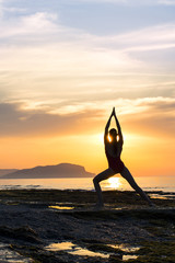 young girl practicing yoga on the beach during the sunset.