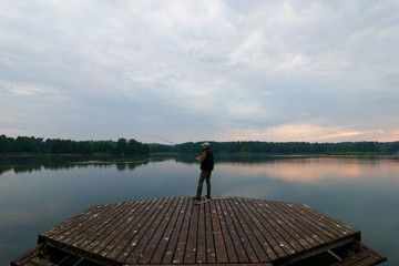 Fisherman catching the fish from wooden pier during cloudy day